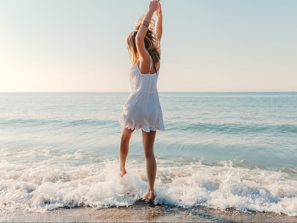 Mujer con vestido blanco bailando a la orilla del mar