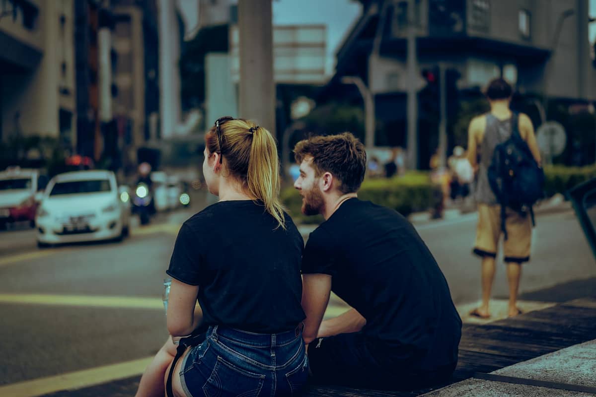 Pareja de mujer y hombre jovenes charlando sentados en una calle de la ciudad