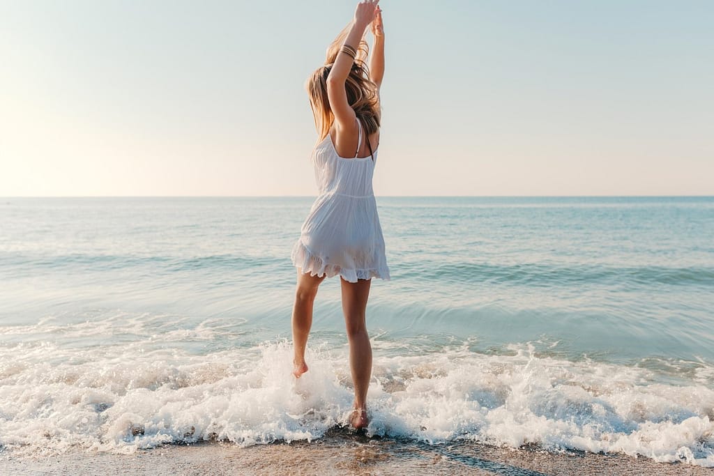 Mujer con vestido blanco bailando con las olas a orillas del mar