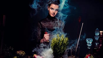 alluring young woman preparing potion against black background